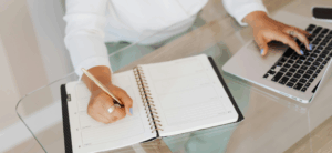 Persona anotando en su agencia y ordenador.