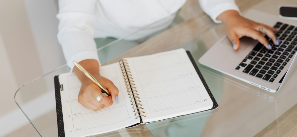 Persona anotando en su agencia y ordenador.